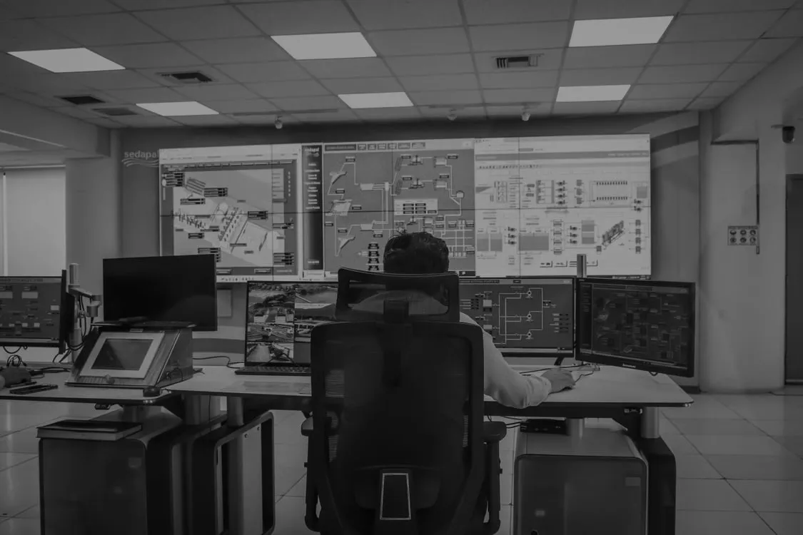 Sala de control con monitores que muestran diagramas y paneles de operación.